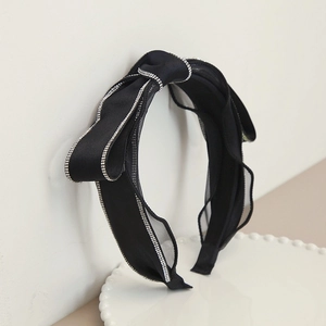 Dettaglio di un cerchietto nero elegante con fiocco e strass luccicanti su raso e mesh