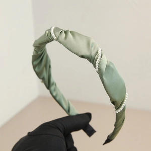 Detail of elegant bean paste green pleated satin headband with white pearl accents
