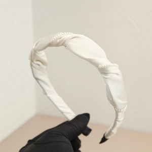 Detail of cream pleated headband with faux pearl embellishments and silky satin fabric
