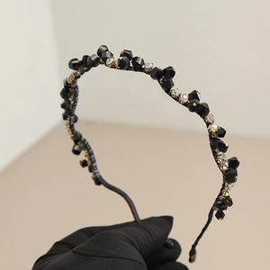 Serre-tête baroque perlé noir avec cristaux tenu par une main gantée