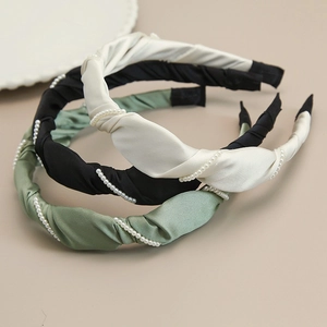 Detailed view of satin twisted headbands with white pearl accents in black, cream, and green