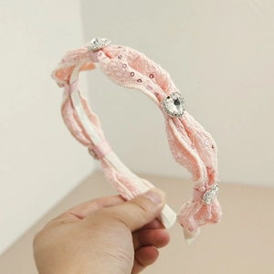 Detail eines rosa Stoff-Haarreifs mit funkelnden Pailletten und großen herzförmigen Kristallen