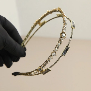 Detail of a gold double-row headband with crystals and grey rhinestones held in hand