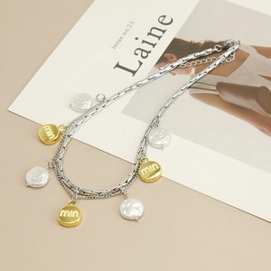 Double-layered geometric necklace with baroque pearl and round letter charm on magazine