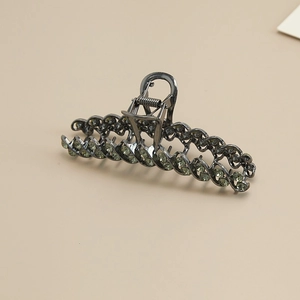 Detail of metal hair claw clip with twisted alloy design and green rhinestone inlay