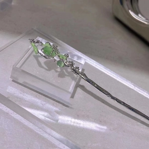 Close-up of silver branch hair pin with green cat eye stones and enamel accents