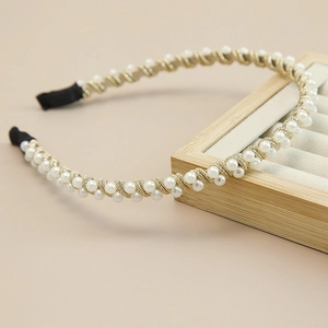 Detail of handcrafted white pearl headband with woven gold wires on a wooden stand