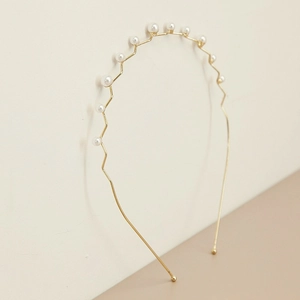 Detail van elegante gouden golvende metalen haarband met witte parels op minimalistische basis