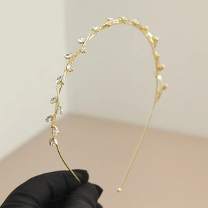 Detailed close-up of a gold vine headband with marquise crystals on a black glove background