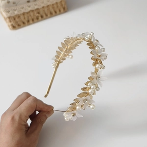 Détail d'un serre-tête doré avec feuilles, fleurs en résine et perles pour mariée