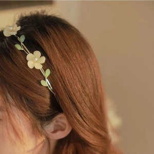 Detail of floral headband with white petals, pearls and green leaves on gold wire