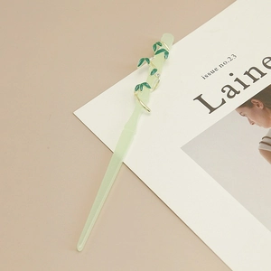 Detailed close-up of bamboo hair stick with green resin flower and golden leaf accents