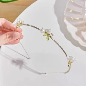 Detail of flower headband with white petals, pearl stamens, and green enamel leaves