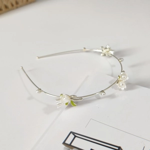Close-up of elegant floral headband with white lily petals, pearls and green leaves