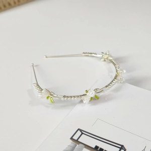 Detail of silver floral headband with white petals, pearls and green leaves on white surface