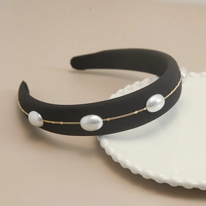 Detail of black sponge headband with gold chain and white pearls on white ceramic plate