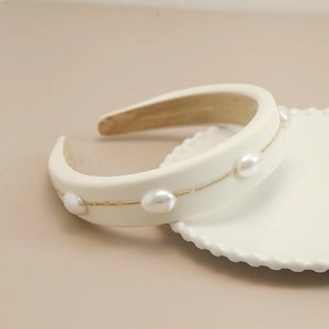 Detail view of cream satin sponge headband with elegant pearls and golden chain decoration