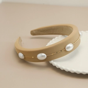 Close-up of beige fabric headband with white pearls and gold chain on ceramic plate