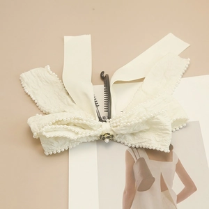 Detalle del clip banana de lazo crema con ribete de perlas y flor de camelia central