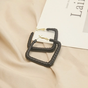 Macro detail of black leather wrap texture on square geometric earrings with gold clasp