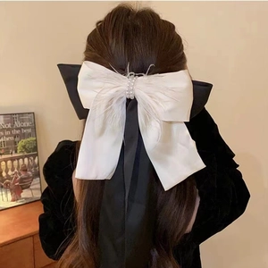 Elegant white feather bow hair clip with pearls and long black streamers on model hair