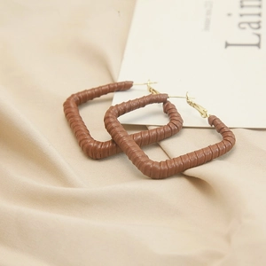Detail of brown faux leather wrapped rectangular earrings with gold needles on fabric