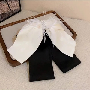 Detail of elegant bow hair clip with white feathers, pearls and long black ribbons