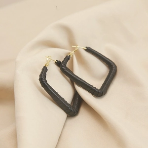 Close-up of black leather wrapped rectangular hoop earrings with gold metal clasp details