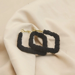 Detailed view of black woven texture rectangular earrings with gold pin closure