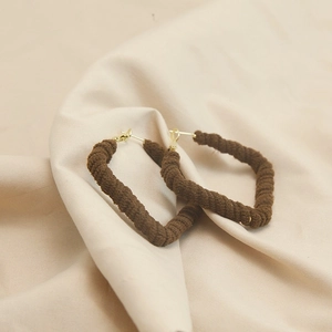 Detail of dark brown yarn-wrapped geometric earrings on soft beige fabric background