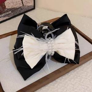 Detailed view of an elegant fabric bow hair clip with white pearls and feathers