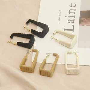 Close-up of rectangular leather-textured hoop earrings in black, beige, and khaki