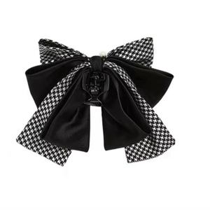 Detail of multilayer houndstooth and black satin bow hair claw with central pearl accent