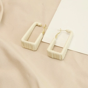 Close-up of rectangle leather earrings in cream white with gold metal hooks and soft texture