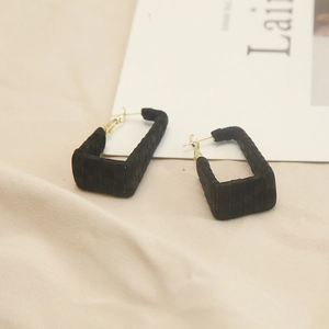 Detail showing rectangular black earrings with vertical pleated texture and golden hooks