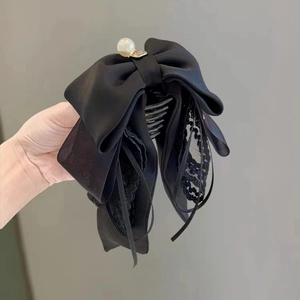 Détail d'une pince à cheveux avec nœud en satin noir, dentelle et perle blanche
