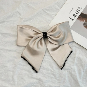 Détail du nœud à cheveux en satin champagne avec bordure en perles noires et texture soie