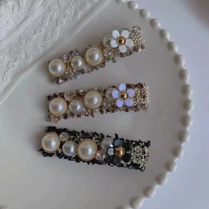 Détail de barrettes en tweed avec perles fantaisie et strass sur fond de dentelle blanche