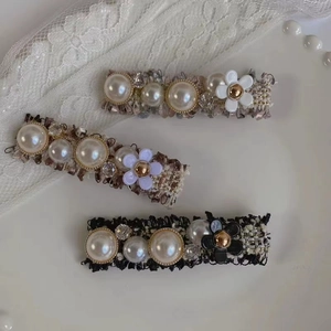 Détail de pinces à cheveux en tweed avec perles et strass sur fond de dentelle blanche