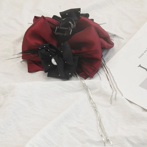 Detail of burgundy satin bow hair claw with black feathers, pearl, and silver rhinestone tassels