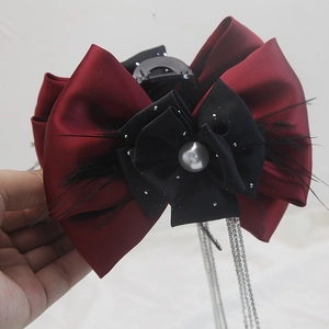Close-up of hair claw clip with burgundy satin bow, black feathers, and rhinestone tassels