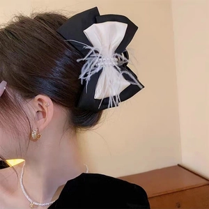 Detail of black fabric bow hair claw clip with white pearls and soft feathers on model