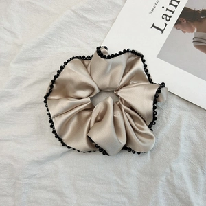 Vue détaillée du chouchou en satin doré champagne avec bordure délicate en perles noires