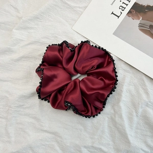 Détail du chouchou en satin bordeaux avec bordure de perles noires et fini soyeux