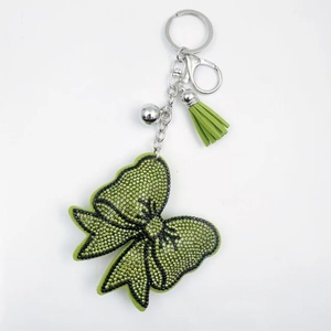 Détail du porte-clés nœud en cristal vert avec clochette et pompon en cuir