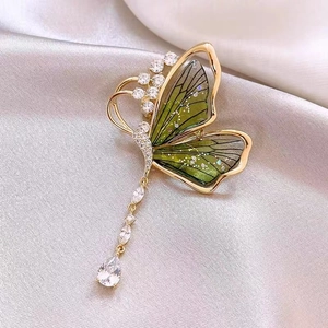 Gros plan d'une broche papillon émeraude avec glands en strass sur tissu en soie