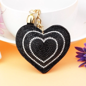 Detail of heart keychain with black rhinestones and gold bell on an orange surface