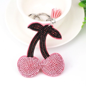 Close-up of pink and black rhinestone cherry keychain with tassel on a white ceramic bowl