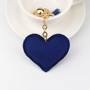 Detail of a navy blue plush heart keychain with gold chain and matching tassel on a white cup