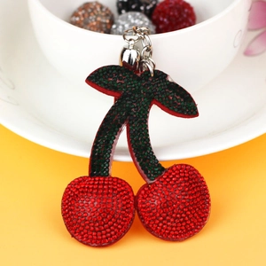 Macro detail of red rhinestone cherry keychain with green crystal leaves on a white cup